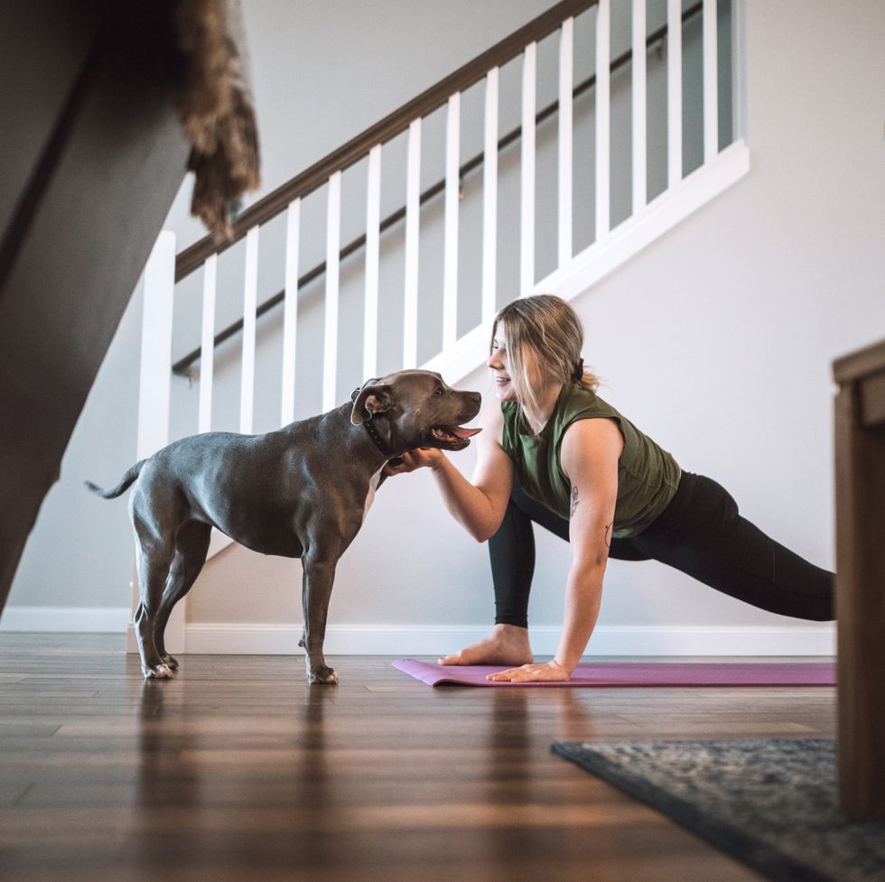 woman at home doing lunges on yoga matt while stroking dog