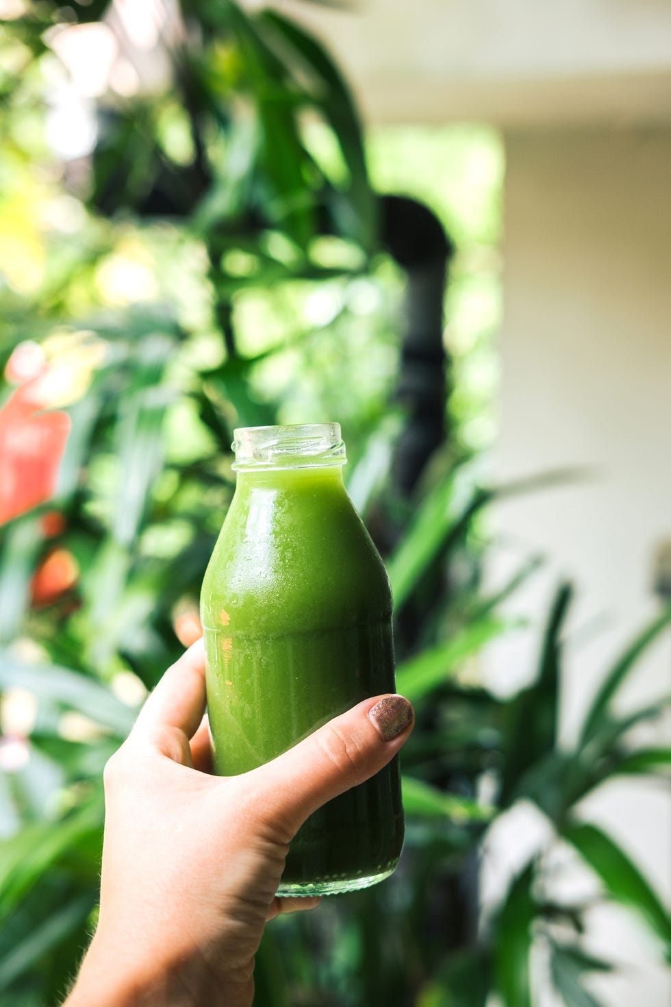 Woman's hand holding a bottle with green juice