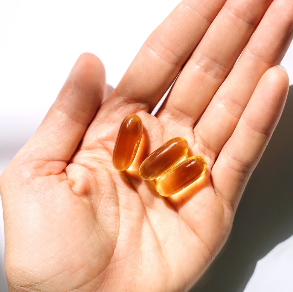 woman's hand holding fish oil supplements on white background