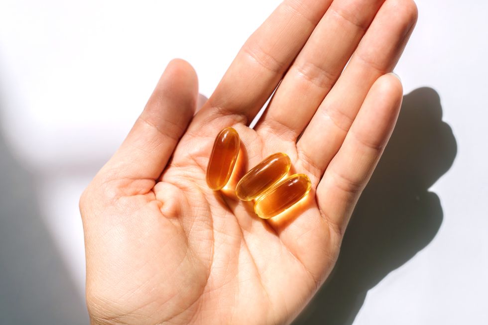woman's hand holding fish oil supplements on white background