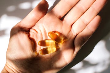 woman's hand holding fish oil supplements on white background