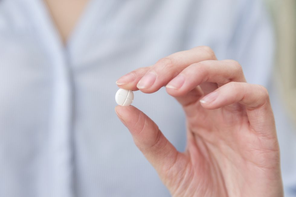 Womans hand holding pill between thumb and forefinger