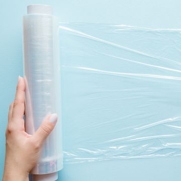 woman's hand using a roll of transparent polyethylene food film for packing products on the pastel blue table empty place for text or logo