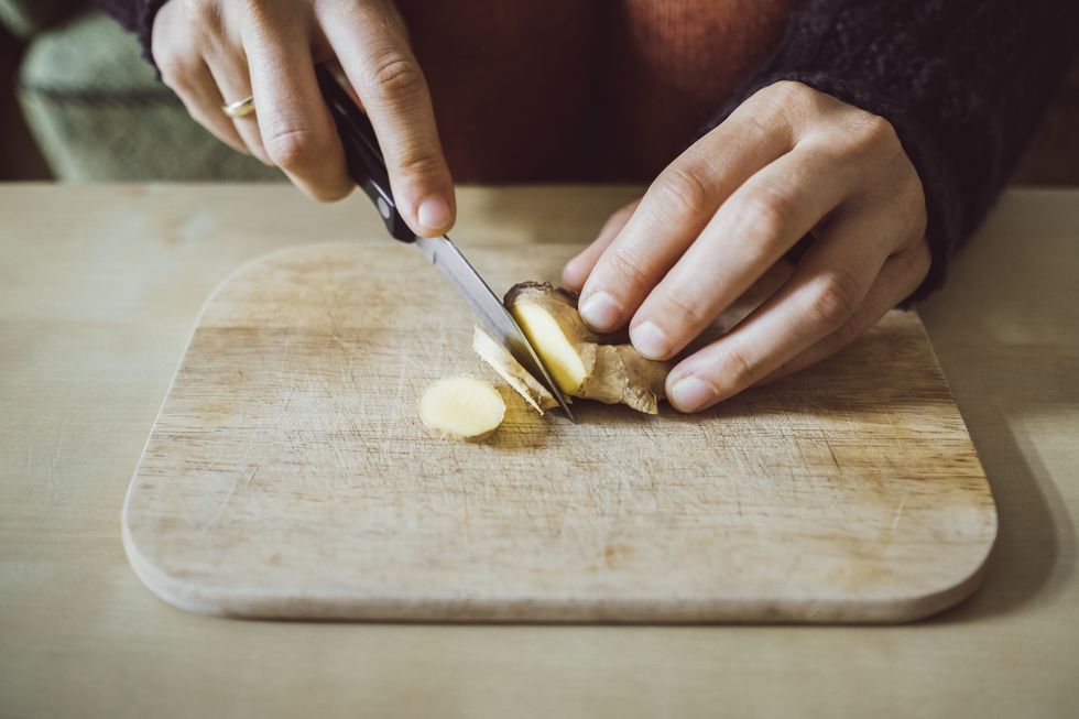 womans hands cutting ginger on wooden board closeup