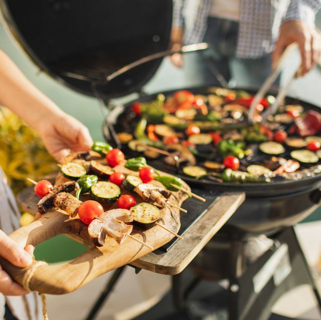 woman's hands holding fresh vegetables on skewers for outdoor barbecue