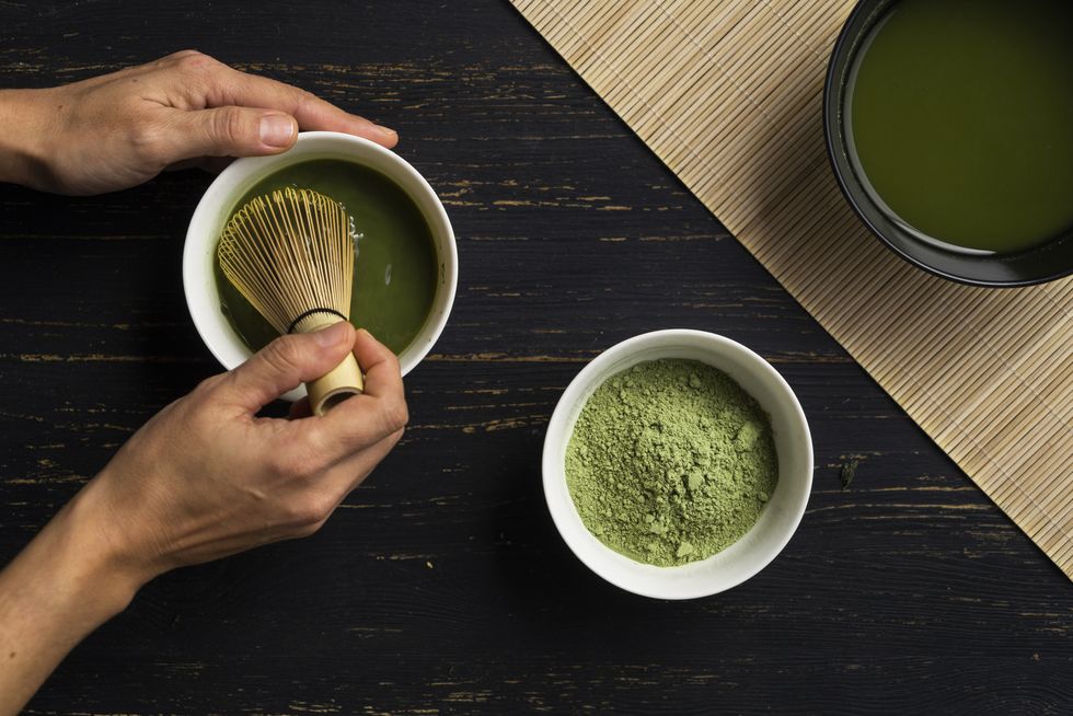 woman's hands mixing matcha green tea powder in a bowl, overhead view