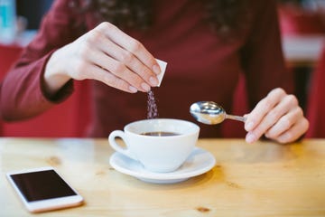 woman's hands pouring sugar into black coffee girl sitting at the table with espresso and smartphone blood and glycemic index control for diabetes excess of white sugar in food concept