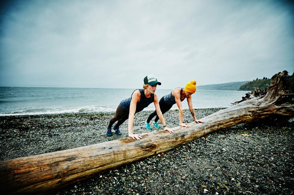 women doing push ups on log on beach