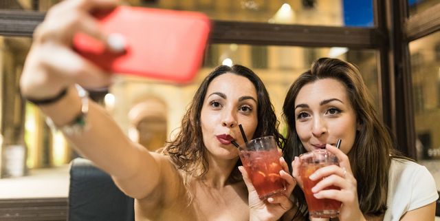Women drinking cocktails taking selfie with smartphone