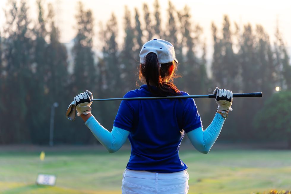 women golfer using golf clubs to help twist to warm up body before the play game, with blurred soft nature background,lifestyle concept sport concept