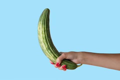 women hand holding cucumber like a man's penis on blue background erotic concept