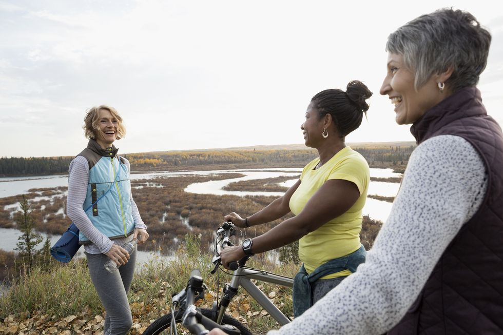 Women with bicycles and yoga mat talking on autumn hilltop overlooking lake