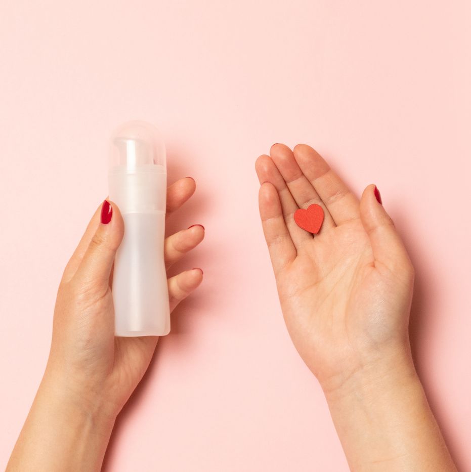 womens hands hold intimate grease and a red heart shape on a pink background