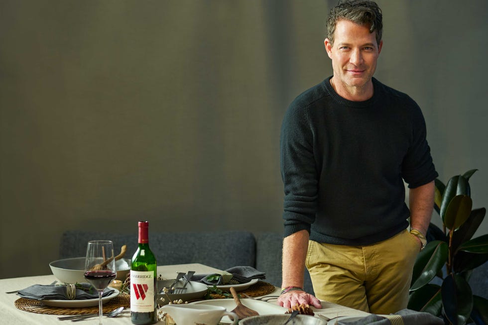 nate berkus standing next to a table set for a meal with wine and dishware