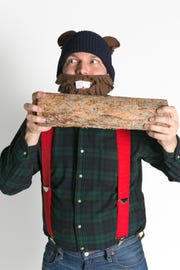 man in funny fleece woodchuck mask and ears wearing red suspenders and flannel shirt pretending to gnaw on log