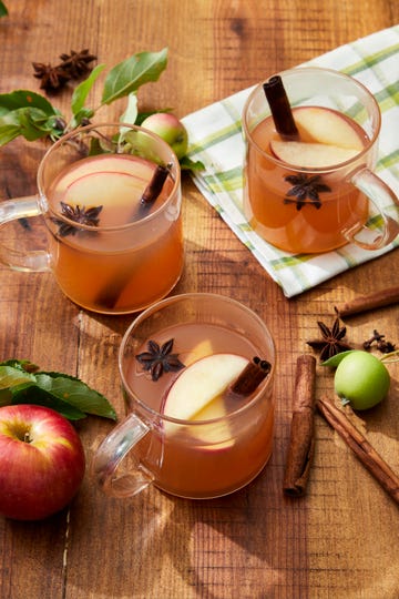 three woodchuck warmer apple cider cocktails in glass mugs with apple star anise and cinnamon sticks for garnish