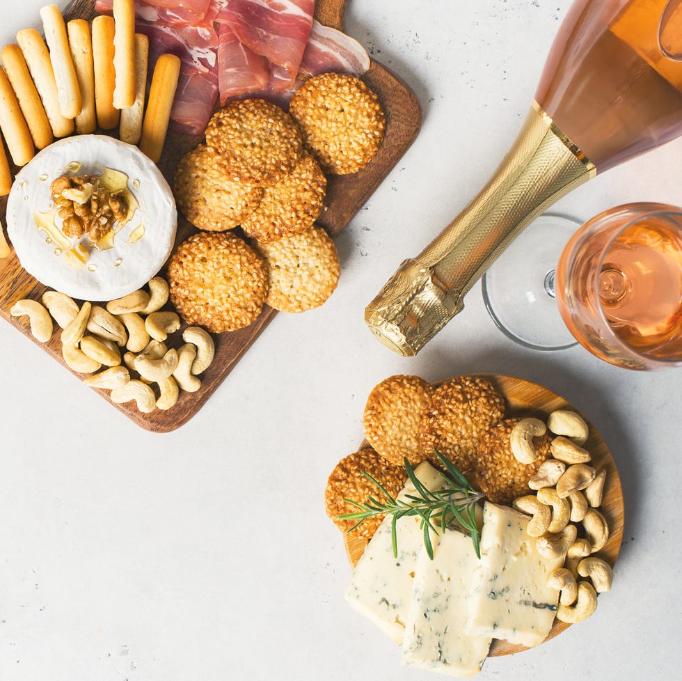 wooden board with cheese, ham, bread stick, nut cashew, walnut and honey on camembert with glasses of wine on white background