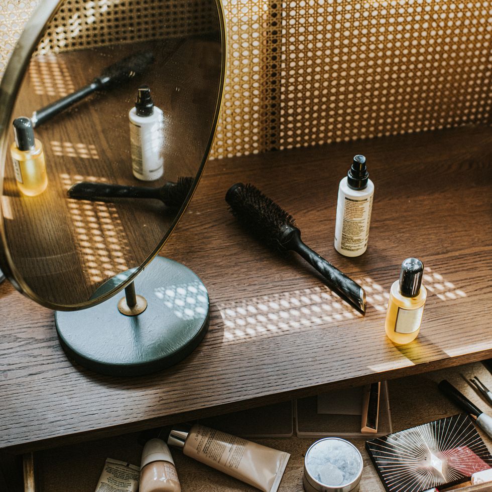 a wooden dressing table in sun with various beauty products, including a hairdryer and diffuser