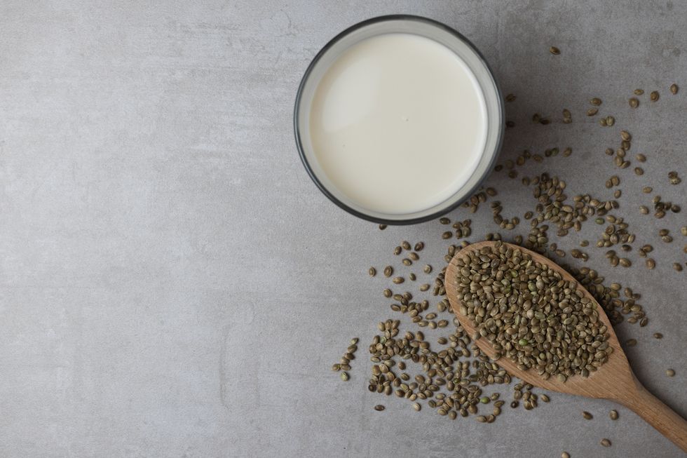 a wooden spoon with hemp seeds and a glass of hemp milk stand on a concrete surface food background