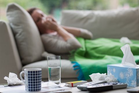 Sick woman laying on sofa blowing nose