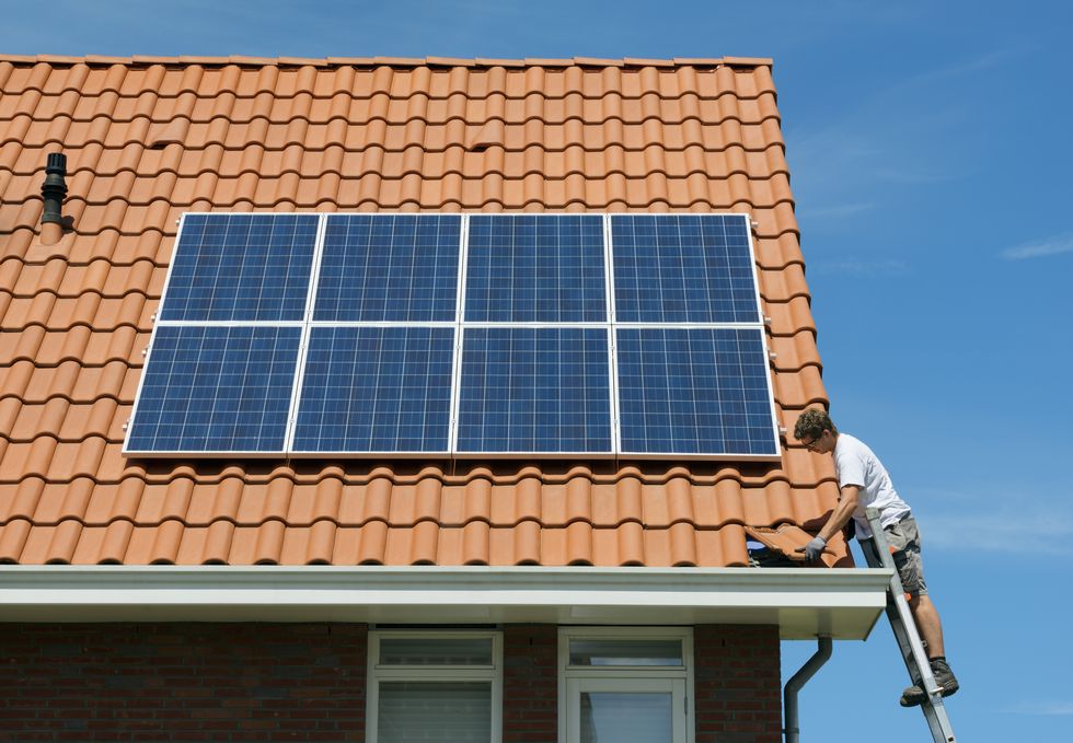 Worker checking installation of solar panels on roof of new home, Netherlands