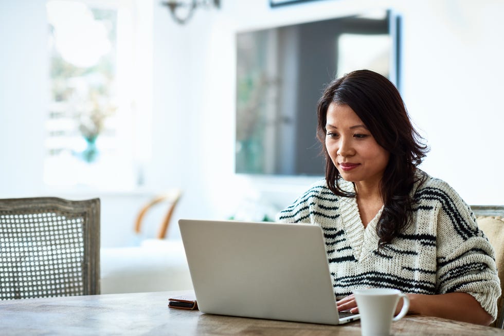 mid adult woman in her 30s sitting at table and looking at computer, remote working, freelancer, small business