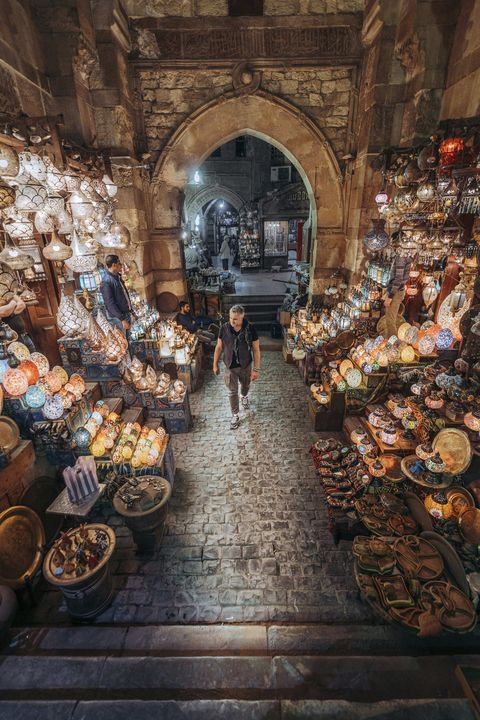 a man walks through a shopping bazaar in cairo egypt and is surrounded by colorful light fixtures and glass wares