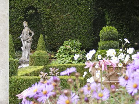 garden statuary among manicured green shrubs with purple flowers in the foreground