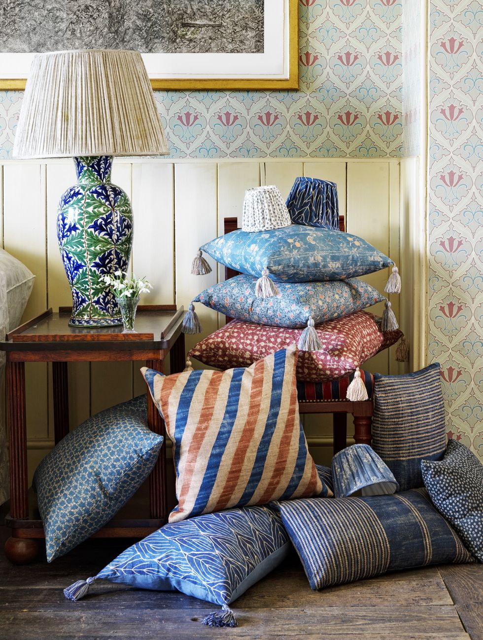 a stack and pile of pillows in different colorful patterns with a blue and green lamp on a table