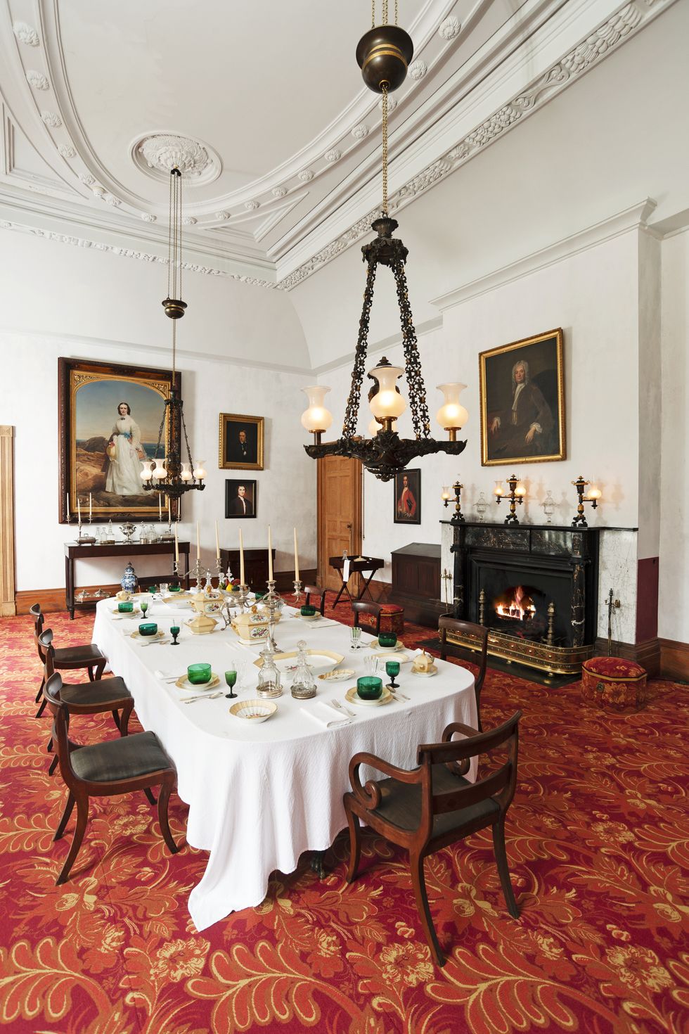 a formal dining room with a a red patterned carpet and oil portraits hanging on the walls
