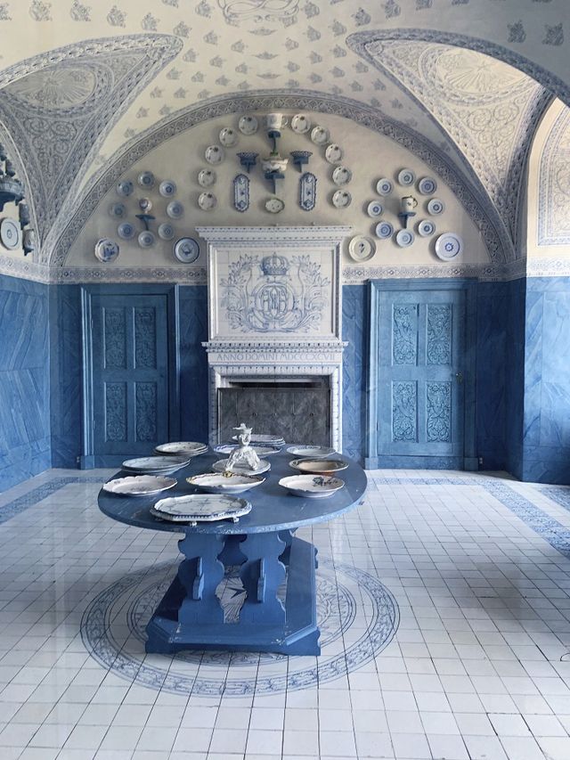 an all blue and white room with plates hung on the wall above a fireplace and a blue wooden table in the middle with a collection of blue and white plates