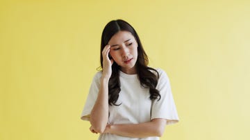 worried asian woman feeling headache on yellow background