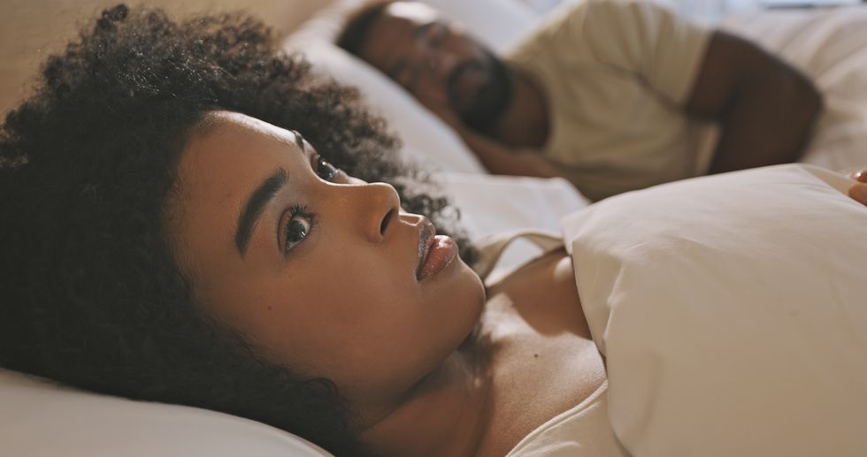 worried black woman laying in bed with insomnia looking anxious and concerned, having infidelity and relationship issues man sleeping while his wife lays awake at night feeling depressed or troubled