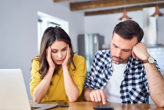 una pareja, preocupada, hace cuentas con la calculadora y el ordenador
