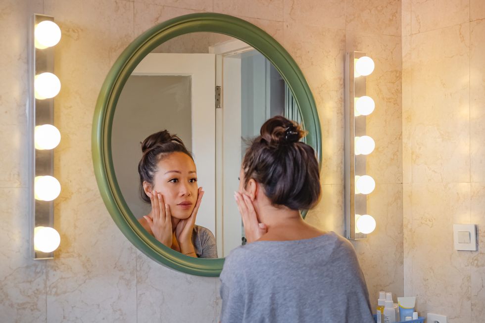 worried east asian woman checking her face skin in the mirror