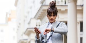 Worried woman standing with smart phone in front of city house