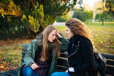 Worried Woman Talking To Friend While Sitting In Park During Autumn