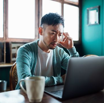 worried young asian man with his hand on head, using laptop computer at home, looking concerned and stressed out