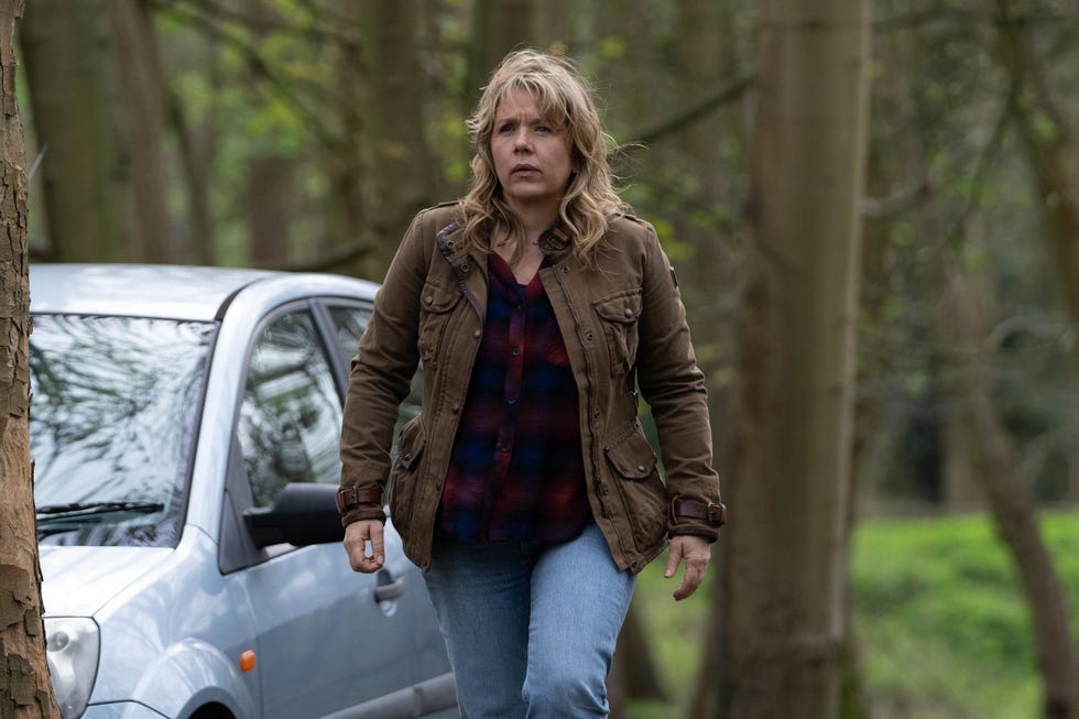 a person walking in a forested area near a parked silver car