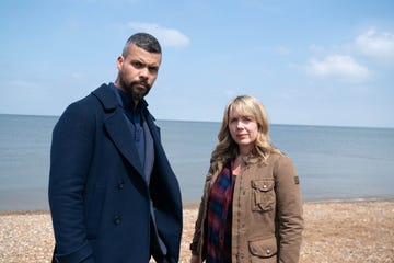 two individuals stand by the beach near the waters edge