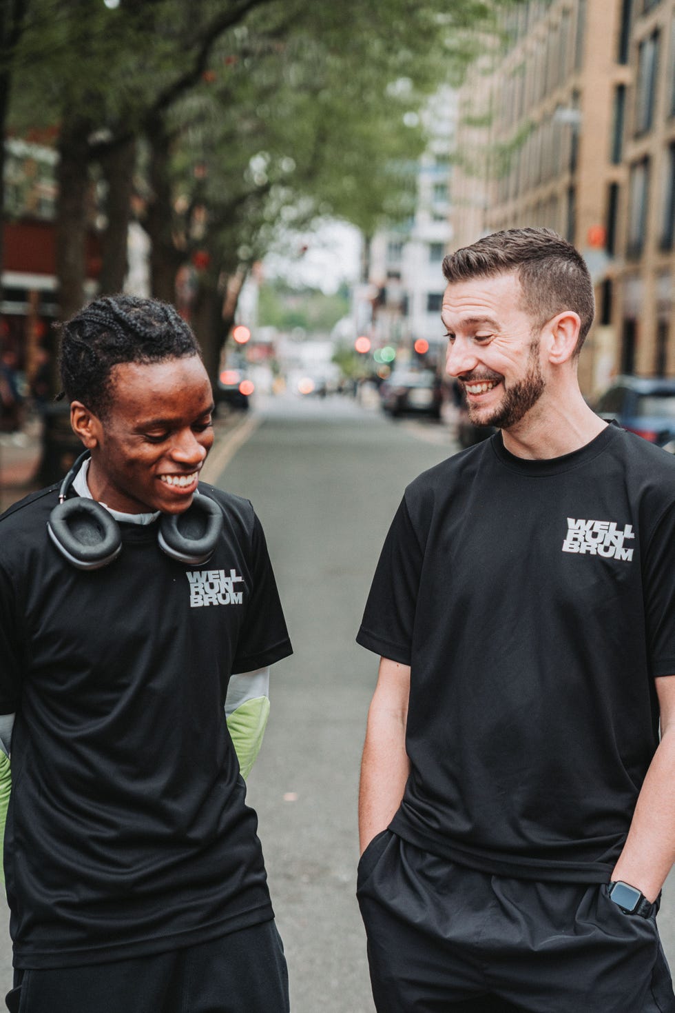 two men wearing running club t shirts smiling together on a road
