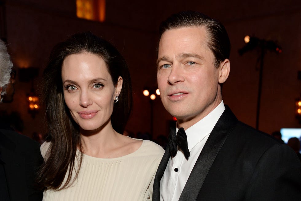 angelina jolie and brad pitt pose together, she wears a cream colored outfit, he wears a black tuxedo and bowtie