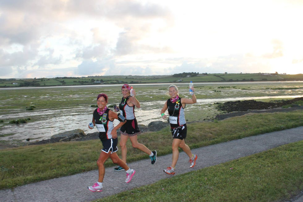 three runners in athletic gear participating in a race by a waterfront
