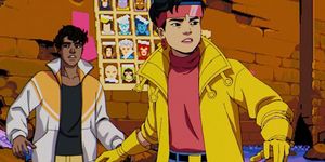 a scared man in a jacket standing behind a brave woman in a bright yellow coat and pink shirt