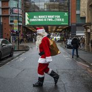 manchester, england   december 02 a man dressed as father christmas walks past covid 19 signage displayed on the arndale in the city centre as manchester enters tier 3 on december 02, 2020 in manchester, england last night mps voted in favour of government proposals to enter england into a tiered system of lockdown beginning at midnight areas in tier three   'very high alert'   sees people not able to meet socially indoors or outdoors with anybody they do not live with or have formed a support bubble with hospitality settings, such as bars, pubs, cafes and restaurants must close except for takeaway, delivery and click and collect services schools remain open photo by anthony devlingetty images