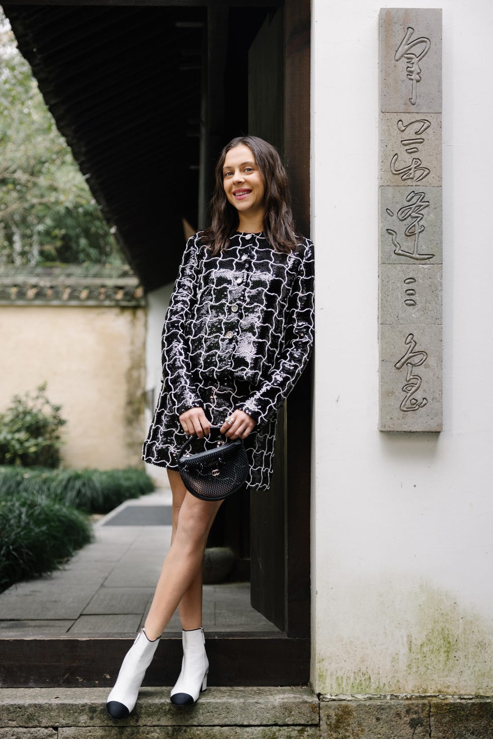 Bel Powney in stylish outfit standing by a doorway in a garden setting