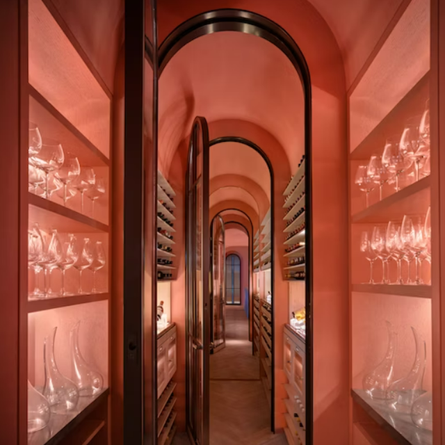 pink hued room view with long skinny arched cofridor with inset shelving on either side for wine and wine glasses and decanters