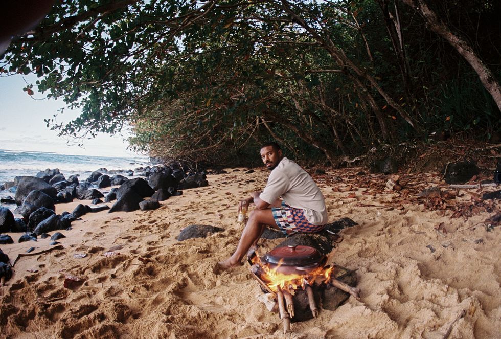 michael b jordan holding a bottle of moss by a beach campfire