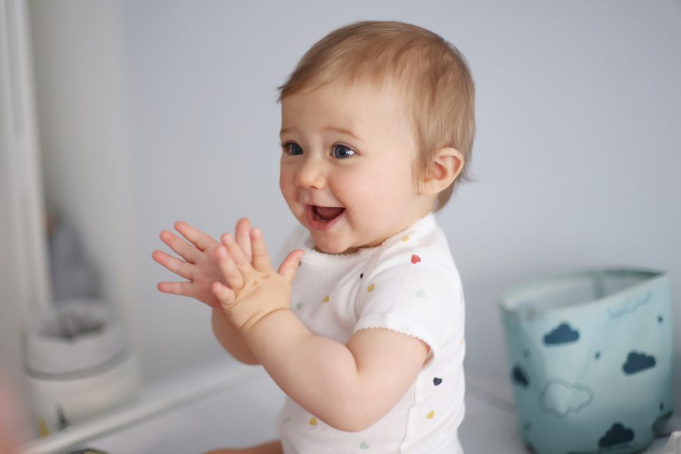 a 1 year old baby girl clapping her hands on her baby changing table