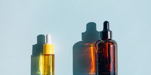 yellow and amber glass bottles with liquid on pastel light blue teal background essential oil or facial serum in vials are used for skin care procedures concept of health spa and wellbeing sunlight makes shadows and illuminating reflections from bottle